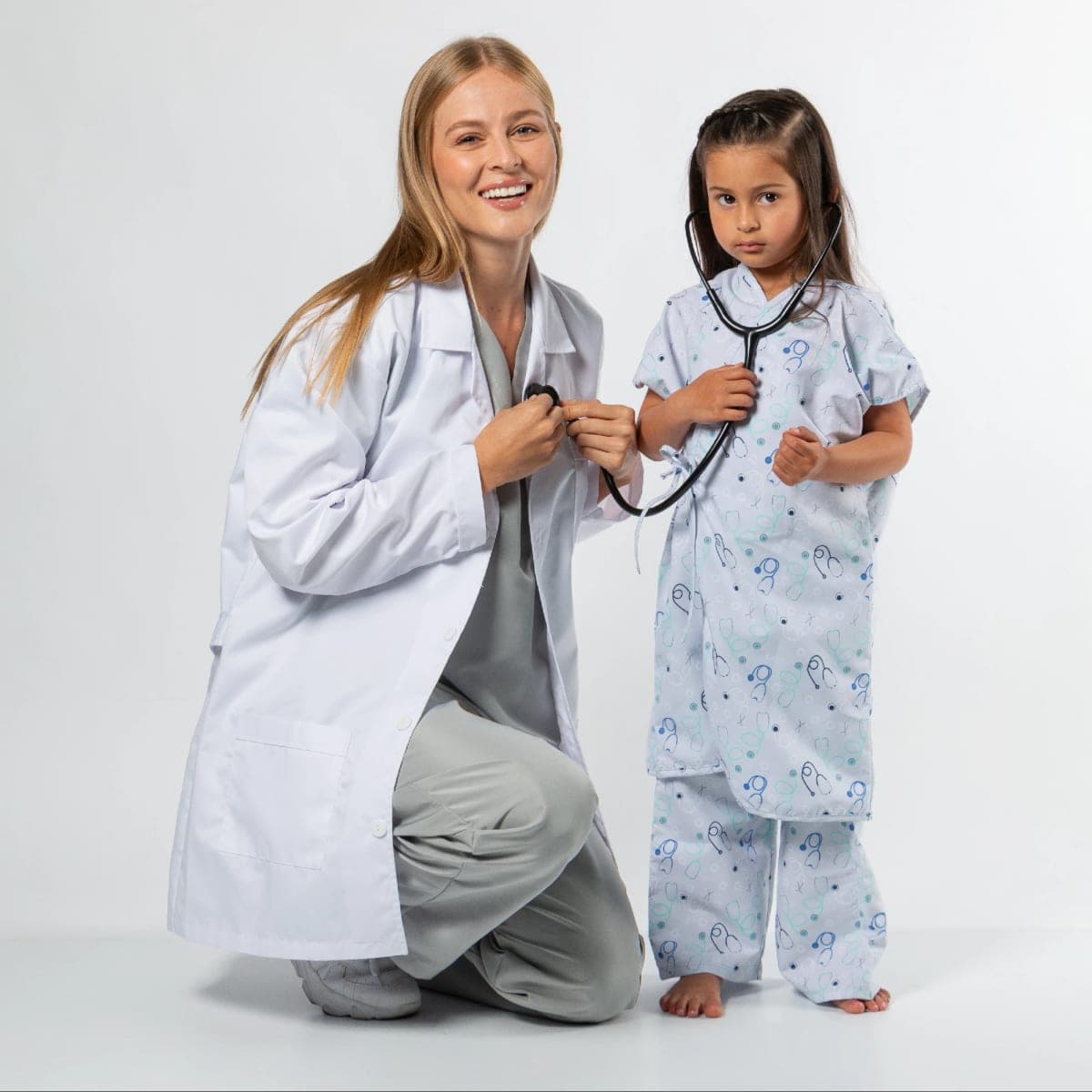 Médica con bata blanca junto a una niña con bata de paciente estampada